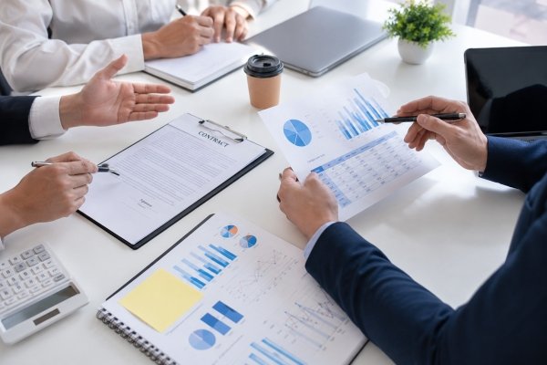AI Image - Corporate team examining financial charts, business reports, and contract documents in a professional office meeting focused on data analysis and strategic decision making.