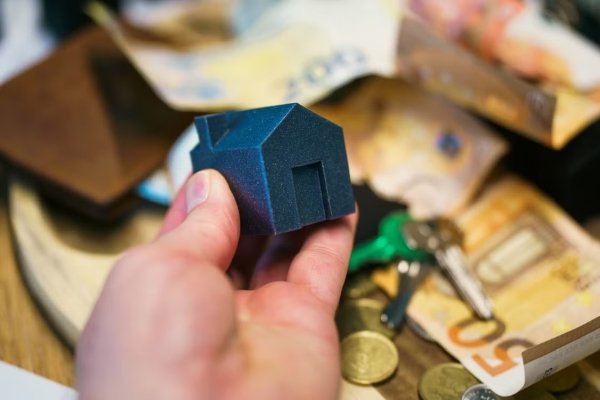 Pexels – Jakub Zerdzicki, Close-up of a hand holding a small house model surrounded by euro banknotes and keys, symbolizing real estate investment