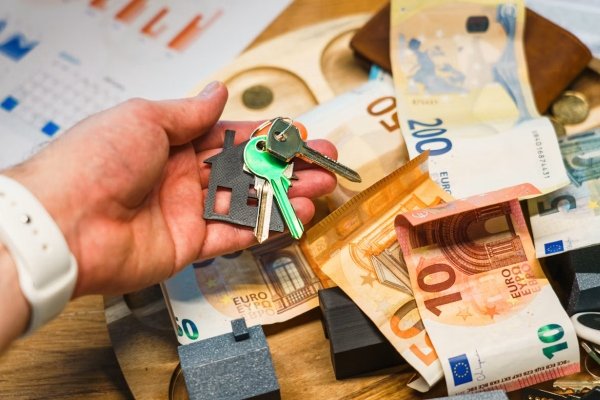 Unsplash – Jakub Żerdzicki, Hand holding house keyes over euro banknotes and charts